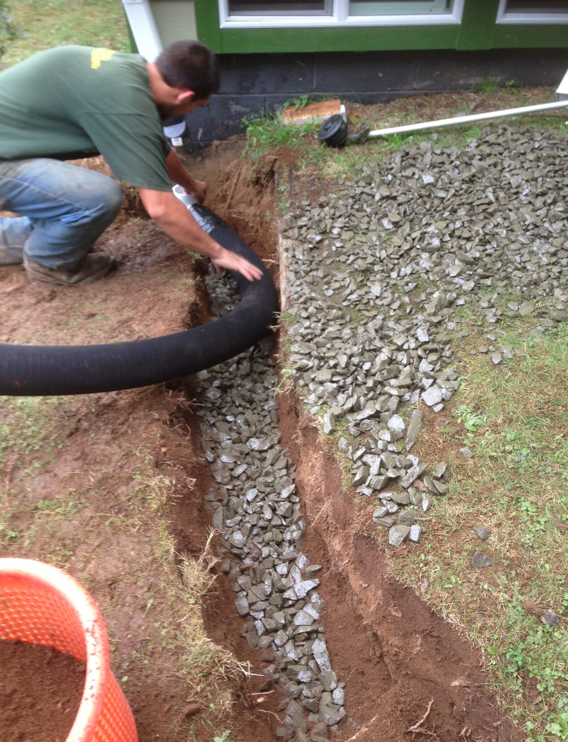 Drainage pipe being installed in a gravel-filled trench beside a home
