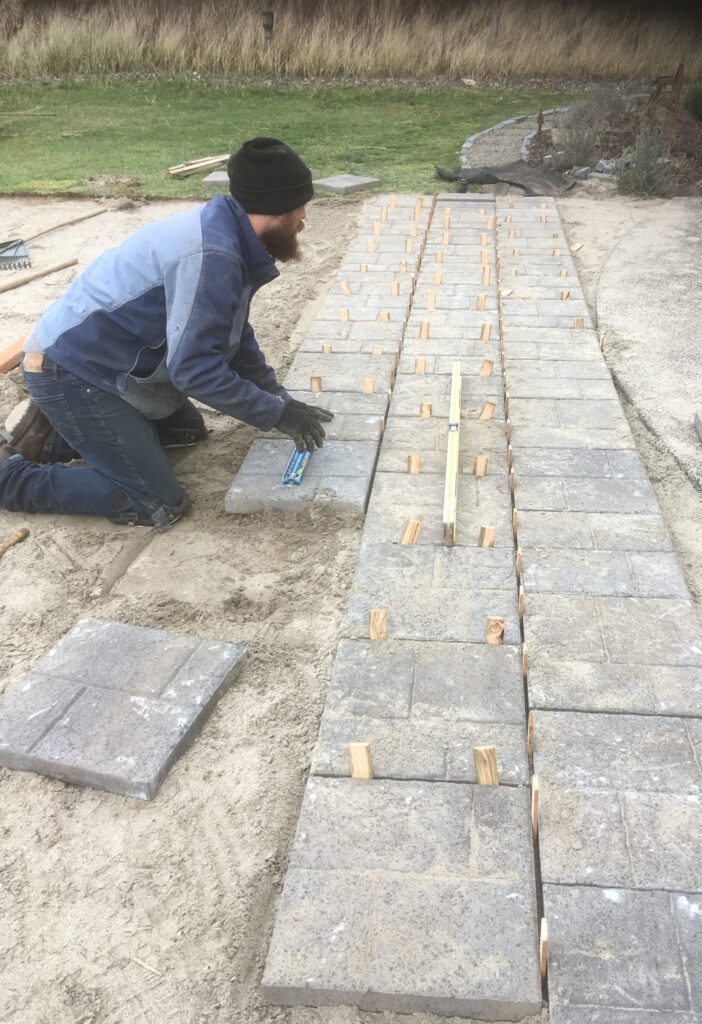 Worker installing and aligning pavers on a prepared sand base - Cannon Beach OR